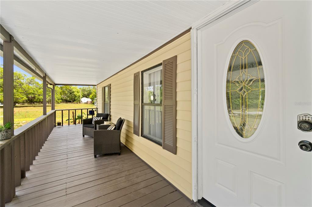 A covered wooden porch features two wicker chairs, yellow siding, and a white front door — 8356 W TAWNY ROSE LANE, CRYSTAL RIVER, FL