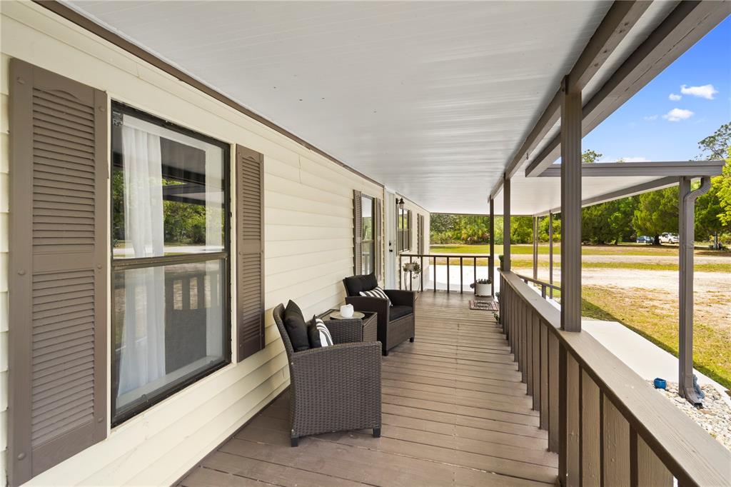 A covered wooden porch with two wicker chairs runs along the side of a house — 8356 W TAWNY ROSE LANE, CRYSTAL RIVER, FL