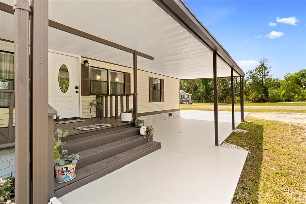 A covered concrete patio and wooden porch steps lead to the front door of a home — 8356 W TAWNY ROSE LANE, CRYSTAL RIVER, FL