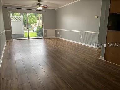 An empty living room features wood-look flooring, light gray walls, wainscoting, and a sliding glass door — 1695 LEE ROAD UNIT C103, WINTER PARK, FL