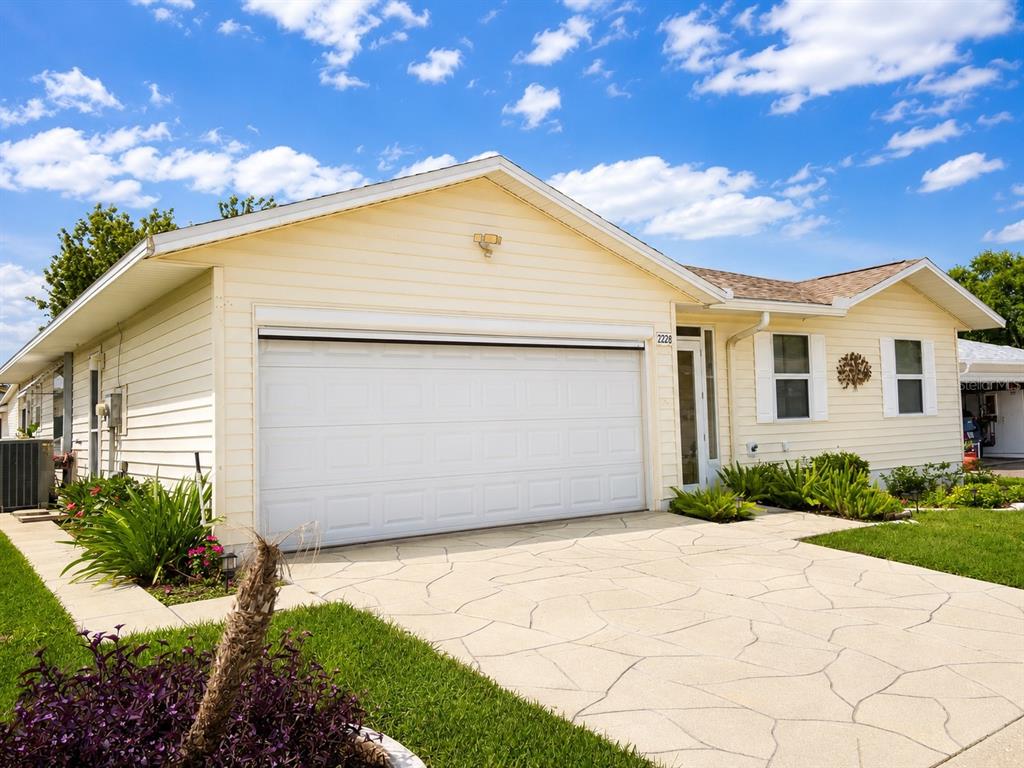 A single-story house with light yellow siding, a white garage door, and a paved driveway — 2228 GRAND CYPRESS DRIVE, LAKELAND, FL
