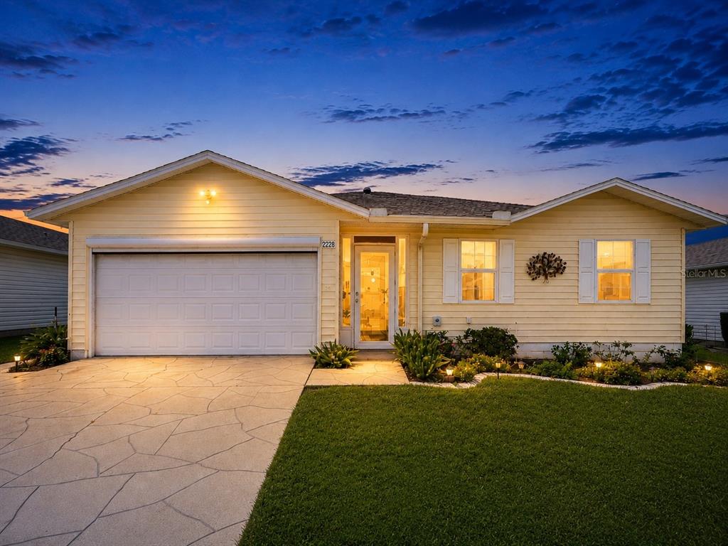A single-story yellow house with a two-car garage and a paved driveway at dusk — 2228 GRAND CYPRESS DRIVE, LAKELAND, FL
