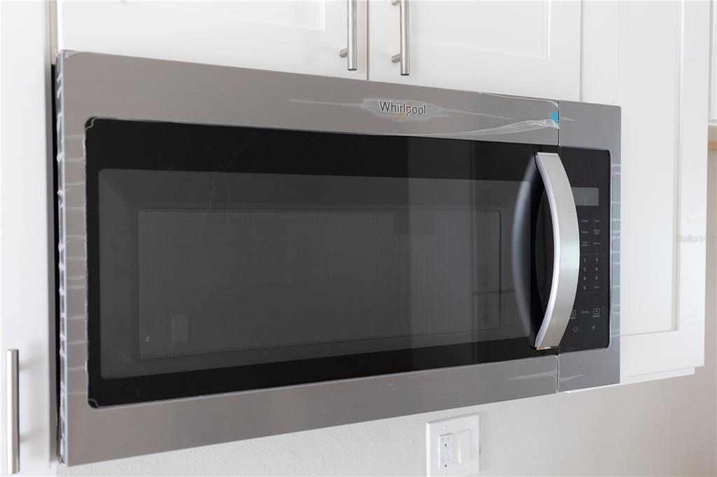 A stainless steel Whirlpool over-the-range microwave is mounted beneath white kitchen cabinets — 1740 2ND STREET NE, WINTER HAVEN, FL