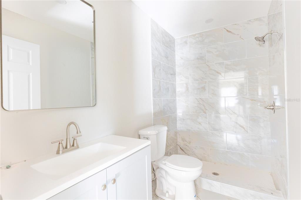 A bathroom features a white vanity, a toilet, and a walk-in shower with marble-look tiles — 1740 2ND STREET NE, WINTER HAVEN, FL