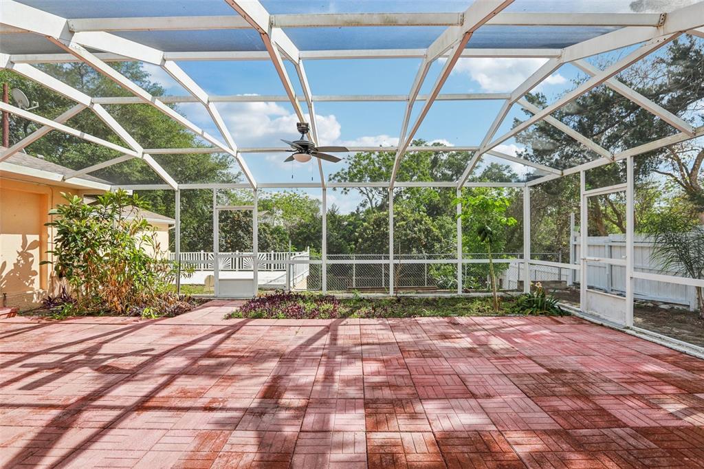 A screened-in patio features red brick pavers, a ceiling fan, and a small garden bed — 1576 OHIO AVENUE, PALM HARBOR, FL