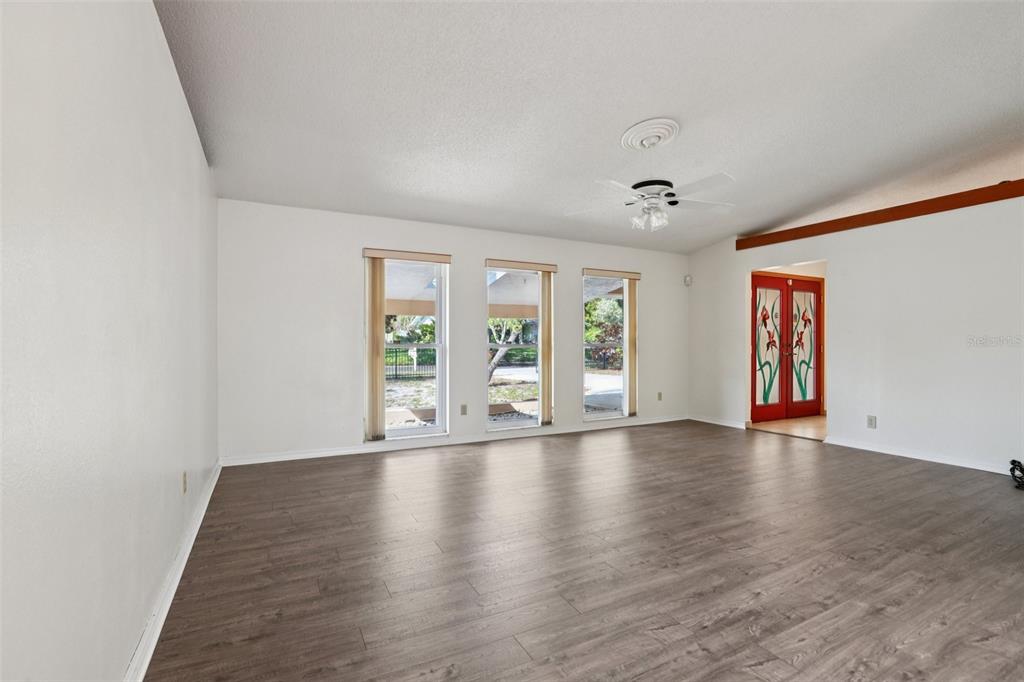 A spacious living room features wood-look flooring, white walls, three windows, and a ceiling fan — 1576 OHIO AVENUE, PALM HARBOR, FL
