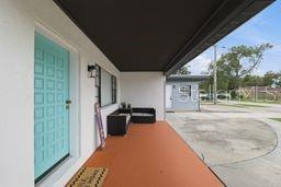 A covered porch features a bright blue front door, orange flooring, and outdoor seating — 2607 W CREST AVENUE, TAMPA, FL