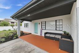 A covered front porch features a painted orange floor, a light blue door, and outdoor furniture — 2607 W CREST AVENUE, TAMPA, FL