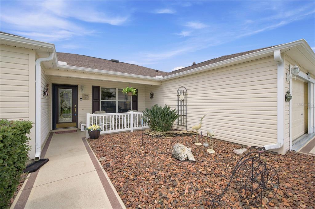 A beige house exterior features a front porch, a gravel yard, and a concrete walkway — 3455 SIPSEY STREET, THE VILLAGES, FL