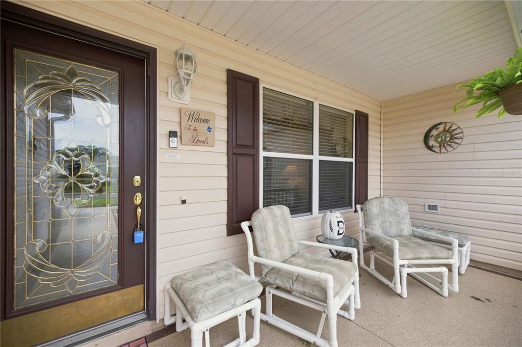 A covered front porch features a decorative glass door, two chairs, and a small table — 3455 SIPSEY STREET, THE VILLAGES, FL