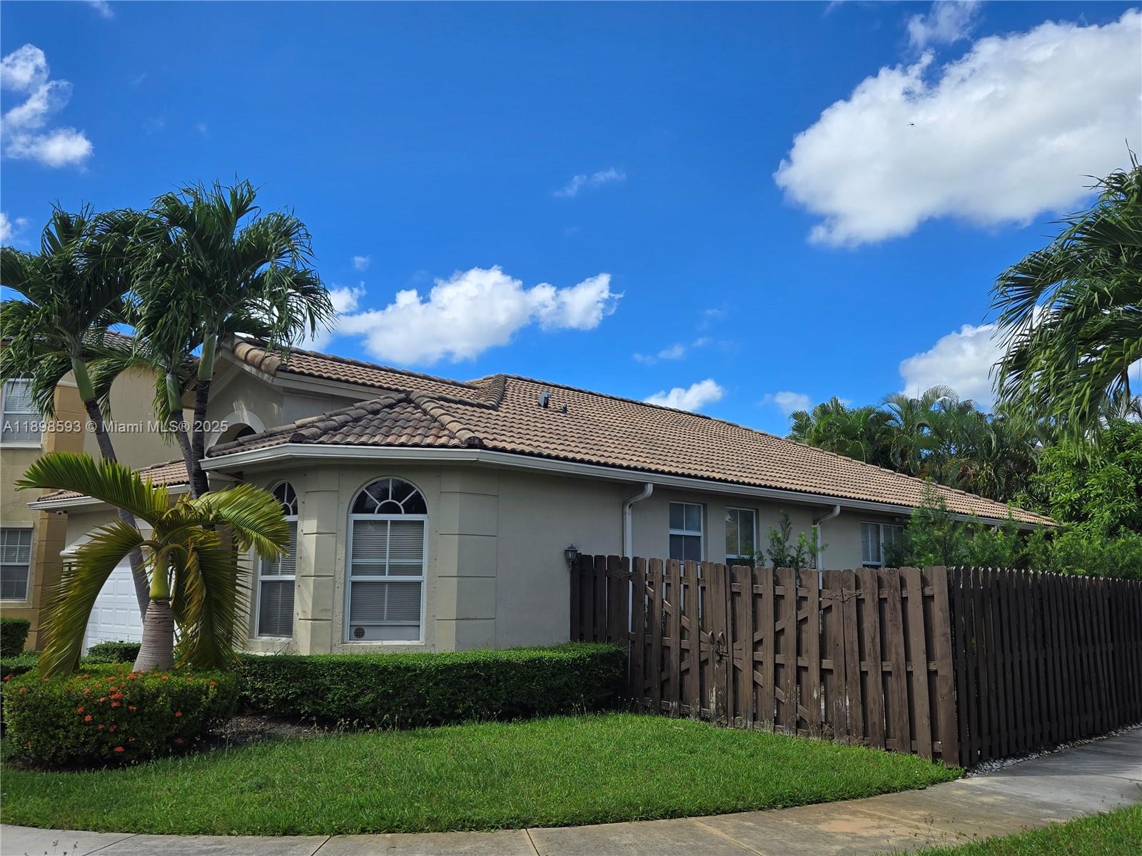 A single-story house with a tiled roof, beige stucco walls, and a wooden privacy fence — 11141 NW 77th Ter, Doral FL 33178, DORAL, FL