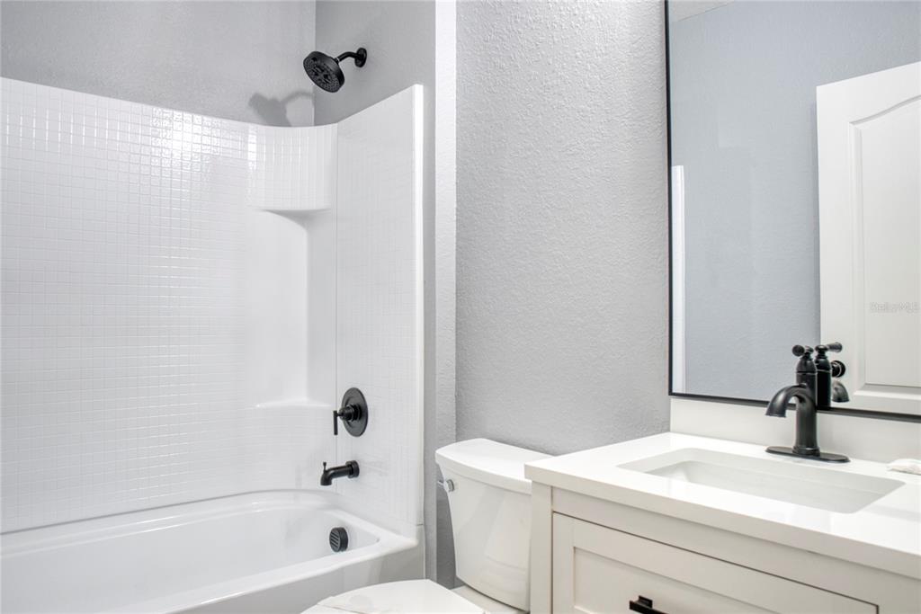 A bathroom features a white tub-shower combo, a white vanity, and black hardware — 3711 JULIUS ESTATES BOULEVARD, WINTER HAVEN, FL