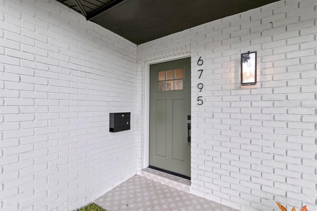 A sage green front door with a window sits in a white painted brick wall — 6795 14TH STREET S, ST PETERSBURG, FL