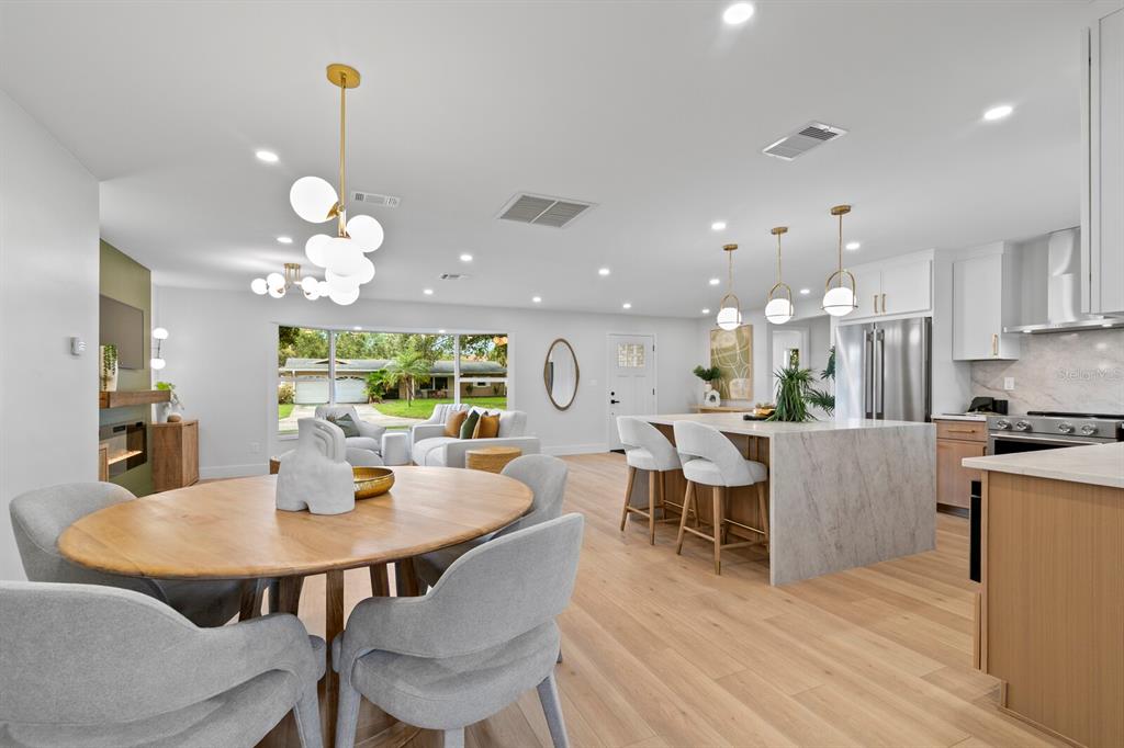 An open-concept kitchen and dining area features light wood flooring, a marble island, and pendant lighting — 6795 14TH STREET S, ST PETERSBURG, FL