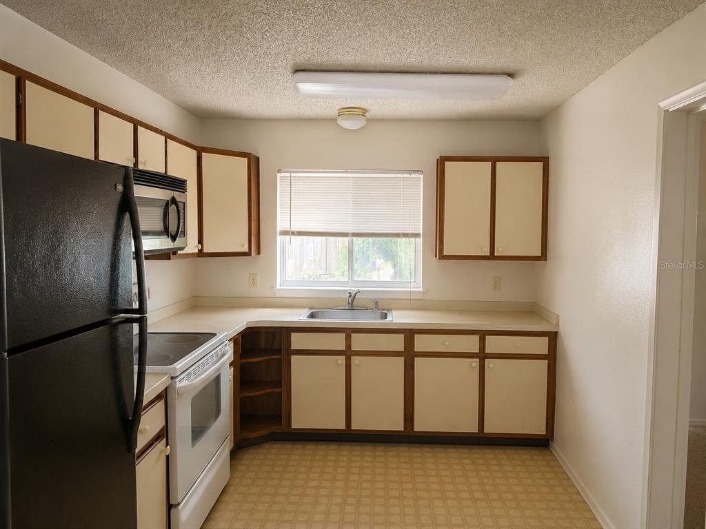 A kitchen with white cabinets, brown trim, a black refrigerator, and a white stove — 8803 PARLIAMENT COURT, KISSIMMEE, FL
