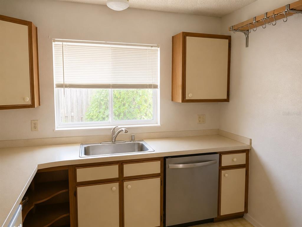 A kitchen features a stainless steel sink, a dishwasher, wood-trimmed cabinets, and a window — 8803 PARLIAMENT COURT, KISSIMMEE, FL