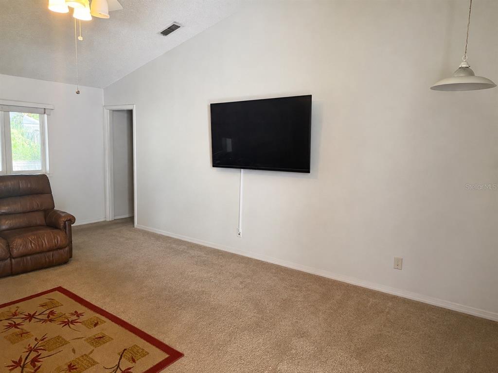 A living room features a wall-mounted television, beige carpeting, and a brown leather recliner — 8803 PARLIAMENT COURT, KISSIMMEE, FL