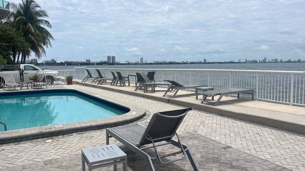 A swimming pool sits on a paved patio overlooking a bay with a city skyline — 2016 Bay Dr # 602, Miami Beach FL 33141, MIAMI BEACH, FL