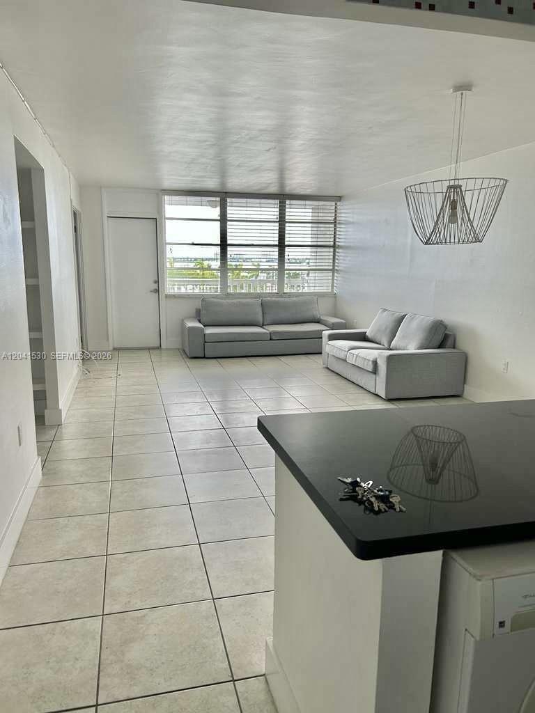 A living room features light tile flooring, two gray sofas, and a wire pendant light — 2016 Bay Dr # 602, Miami Beach FL 33141, MIAMI BEACH, FL