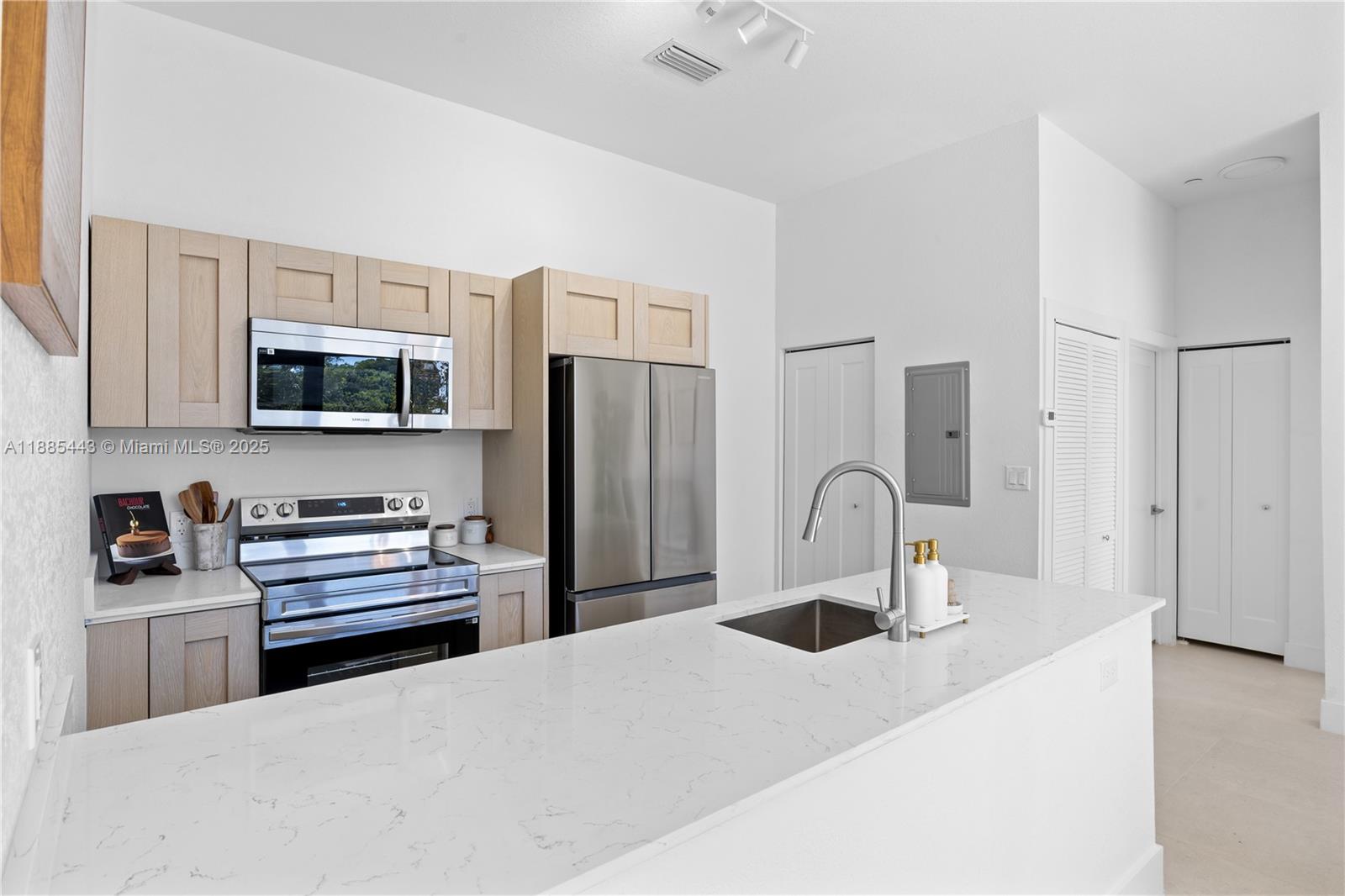 A modern kitchen features light wood cabinets, stainless steel appliances, and a white quartz island — 21850 Old Dixie highway # 001, Miami FL 33170, MIAMI, FL