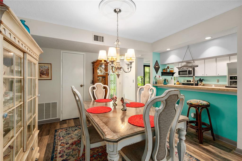 A dining room with a wooden table, chandelier, and an adjacent kitchen with turquoise walls — 1701 PELICAN COVE ROAD UNIT 359, SARASOTA, FL