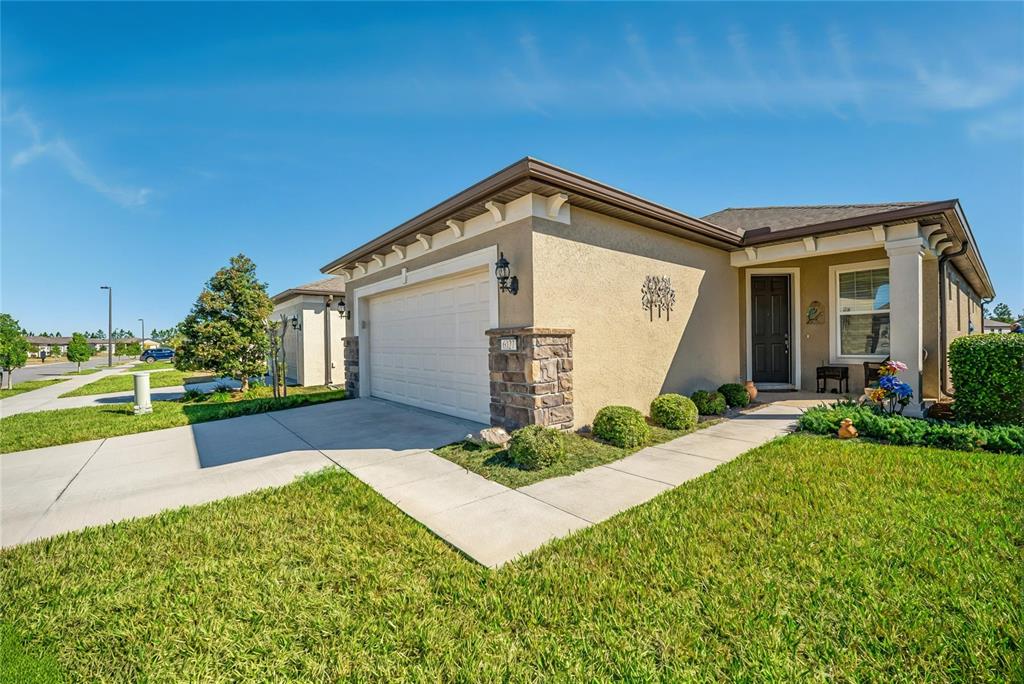 A tan stucco house with a stone-accented garage and a front walkway on a sunny day — 6027 SW 93RD CIRCLE, OCALA, FL