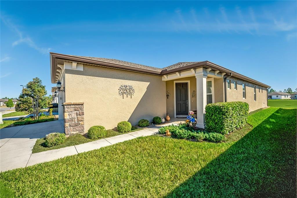 A single-story house with a tan stucco exterior, stone accents, and a covered front porch — 6027 SW 93RD CIRCLE, OCALA, FL