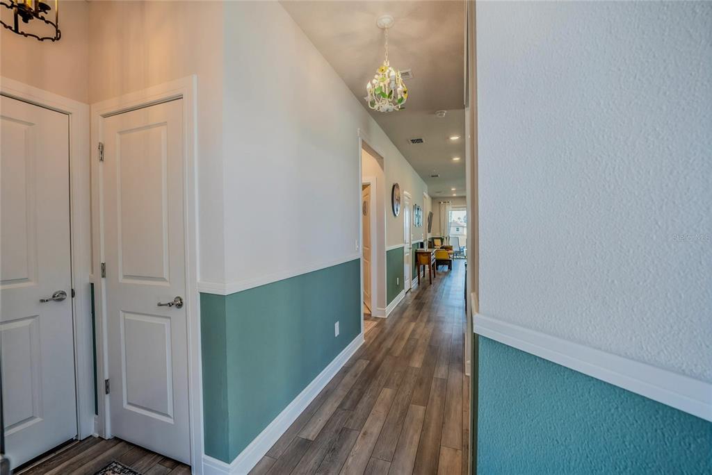 A hallway with wood-look flooring, teal wainscoting, and a decorative chandelier leads to a living area — 6027 SW 93RD CIRCLE, OCALA, FL