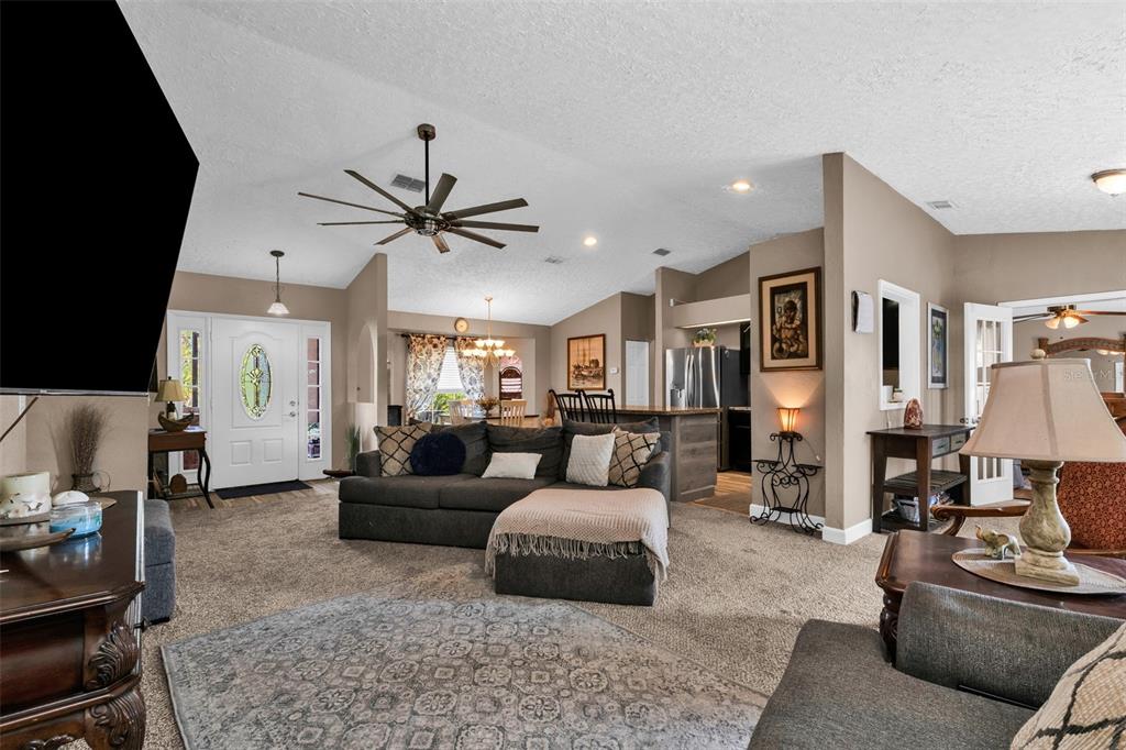 A living room with a sectional sofa, ceiling fan, and an open view to the kitchen — 2210 EMBASSY ROAD, NORTH PORT, FL