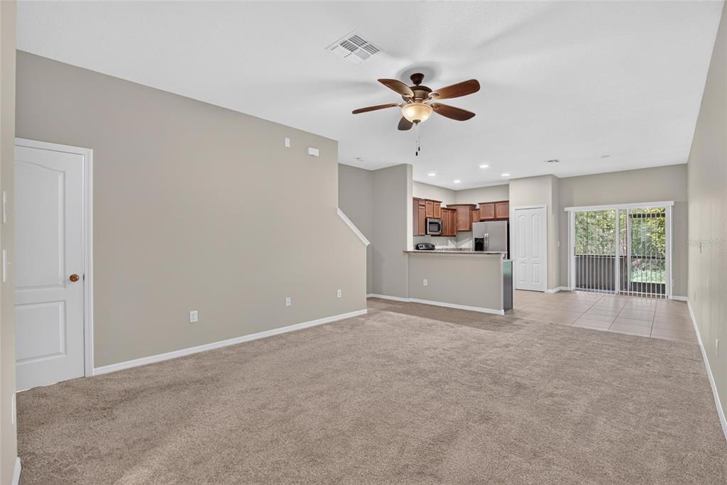 An open-concept living room with beige carpet, a ceiling fan, and an adjacent kitchen area — 2829 SANTEGO BAY COURT, BRANDON, FL