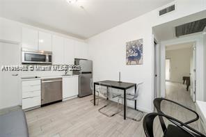 A modern kitchen features white cabinetry, stainless steel appliances, and a small dining table — 820 15th St # 104, Miami Beach FL 33139, MIAMI BEACH, FL
