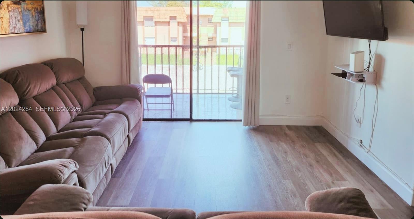 A living room with wood-look flooring, a brown sofa, and a sliding glass door balcony — 6480 W 27th Ct # 22, Hialeah FL 33016, HIALEAH, FL