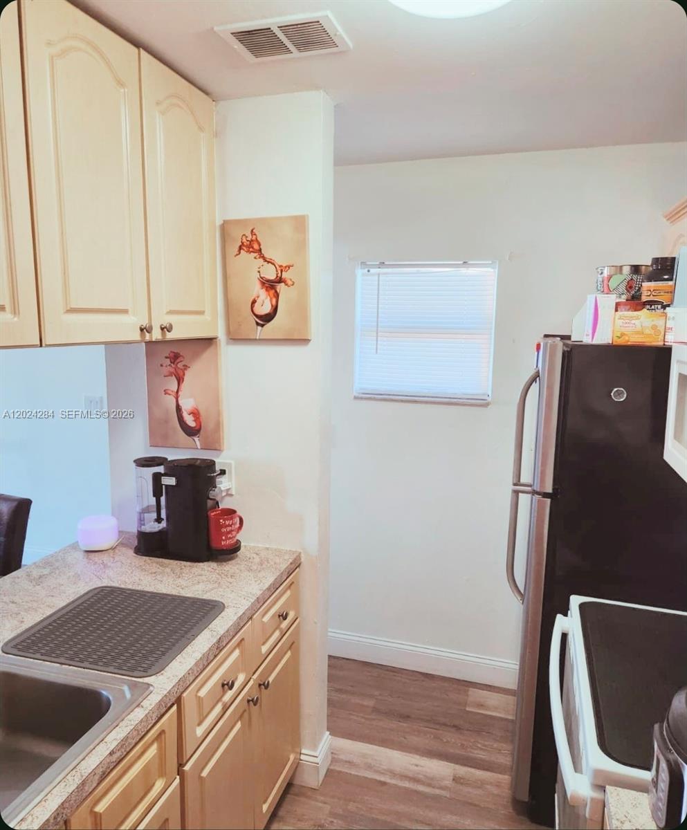 A kitchen features light wood cabinets, granite countertops, a black refrigerator, and two wine-themed wall prints — 6480 W 27th Ct # 22, Hialeah FL 33016, HIALEAH, FL