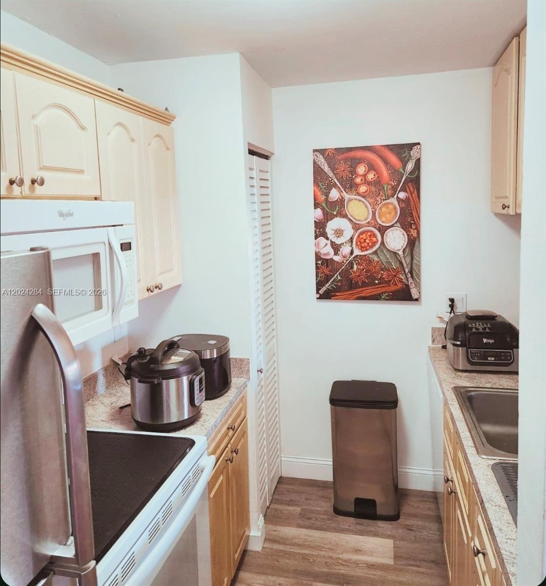 A galley-style kitchen features light wood cabinets, granite countertops, stainless steel appliances, and wood flooring — 6480 W 27th Ct # 22, Hialeah FL 33016, HIALEAH, FL
