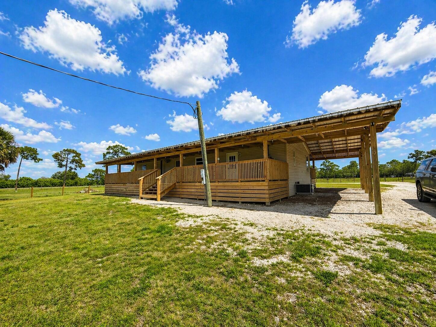 A single-story house with a large wooden deck and attached carport under a blue sky — 1075 SW Rucks Dairy Road, Okeechobee FL 34974, OKEECHOBEE, FL