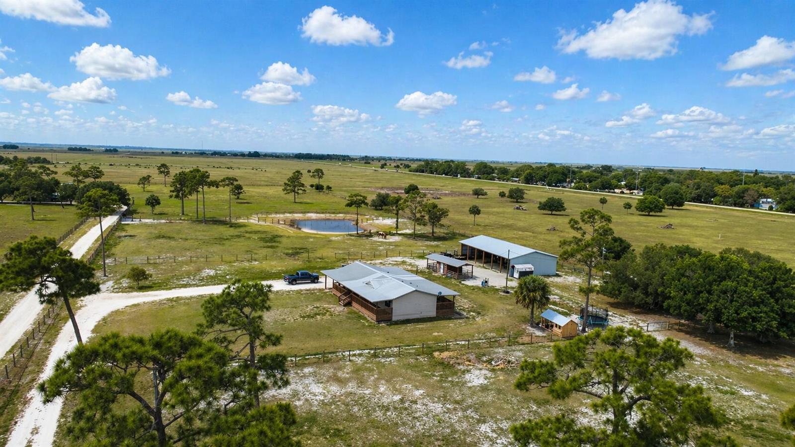 An aerial view shows a house, a large metal barn, and a pond on land — 1075 SW Rucks Dairy Road, Okeechobee FL 34974, OKEECHOBEE, FL