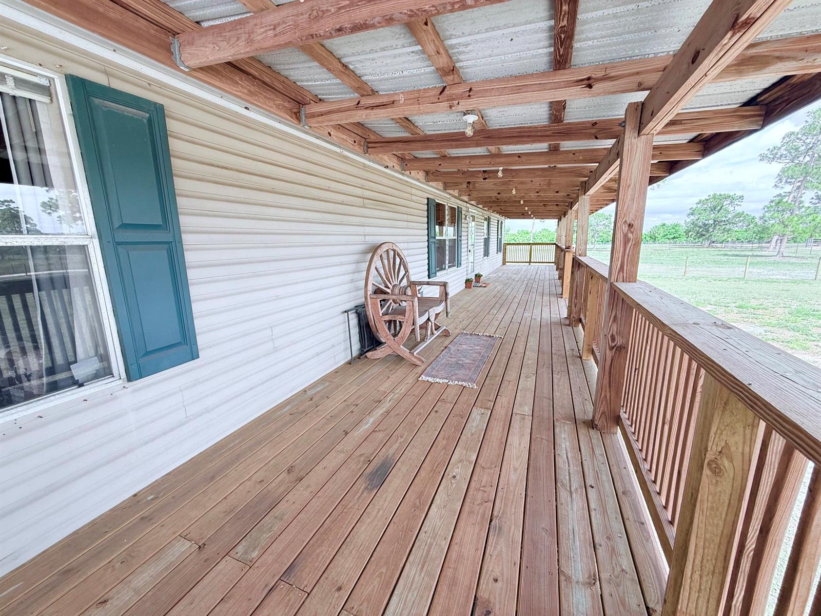 A long wooden porch with a metal roof, railing, and a wagon wheel bench — 1075 SW Rucks Dairy Road, Okeechobee FL 34974, OKEECHOBEE, FL