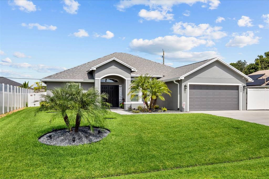A gray single-story house with a two-car garage, palm trees, and a manicured lawn — 1980 SW AMERICANA STREET, PORT ST LUCIE, FL