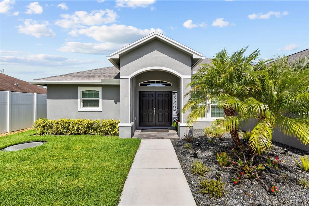 A gray house exterior features a double front door, a walkway, and a palm tree — 1980 SW AMERICANA STREET, PORT ST LUCIE, FL