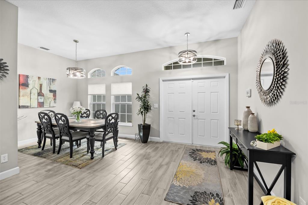 A dining room with a double front door, light wood-look tile floors, and two chandeliers — 1980 SW AMERICANA STREET, PORT ST LUCIE, FL