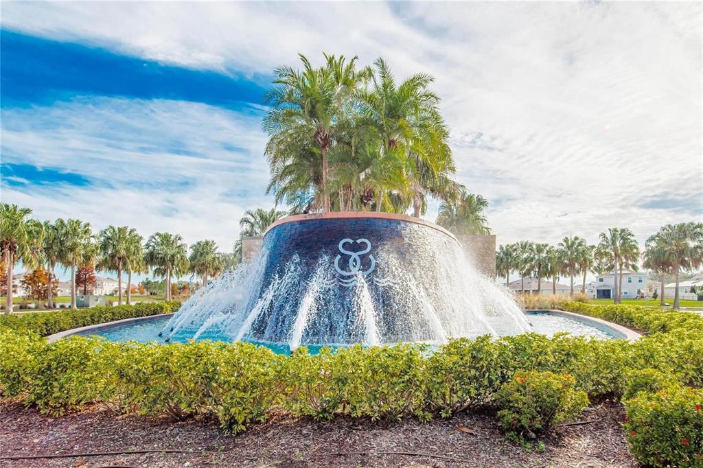 A large, curved water fountain with palm trees sits in front of a residential community — 17029 BLISTER WING DRIVE, WIMAUMA, FL