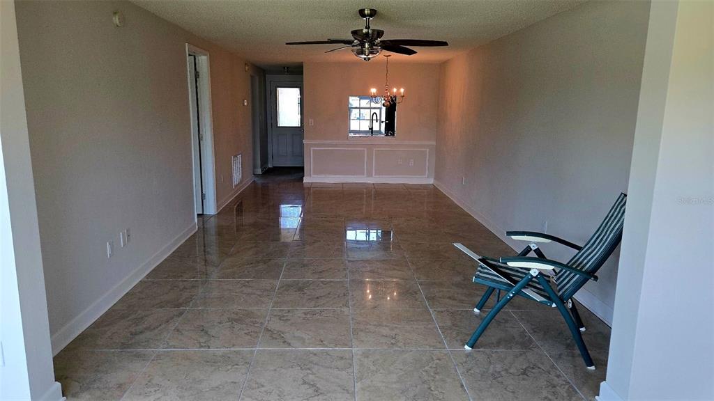 An empty room with tan tile flooring, a ceiling fan, and a single folding chair — 4249 STRATFORD DRIVE UNIT 4249, NEW PORT RICHEY, FL