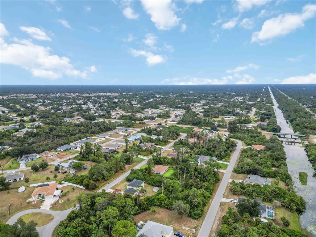 An aerial view shows a suburban neighborhood with houses, wooded areas, and a long canal — 17370 WELLSLEY AVENUE, PORT CHARLOTTE, FL