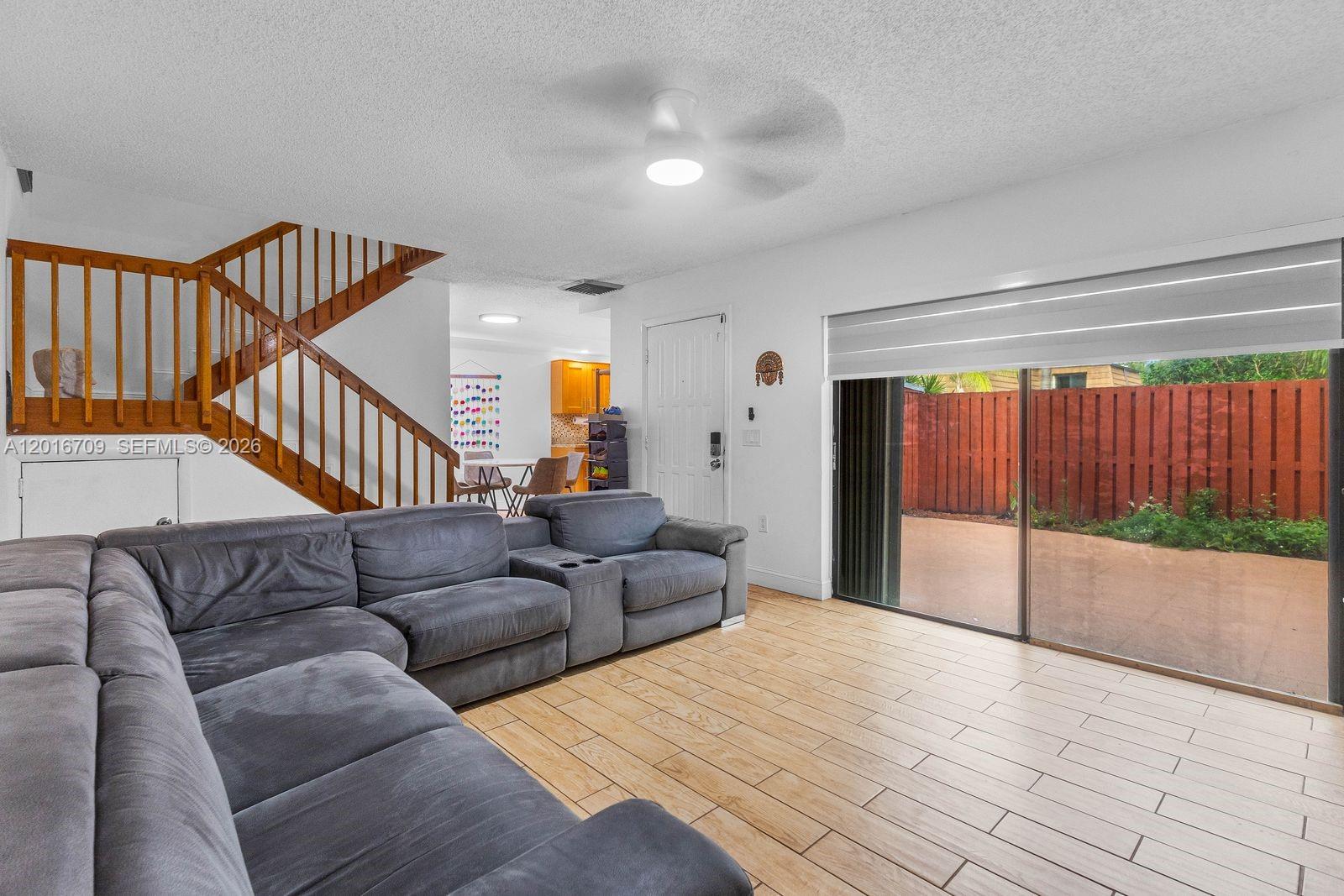A living room features a large gray sectional sofa, wood-look tile floors, and sliding glass doors — 9126 SW 20th Pl # C, Davie FL 33324, DAVIE, FL