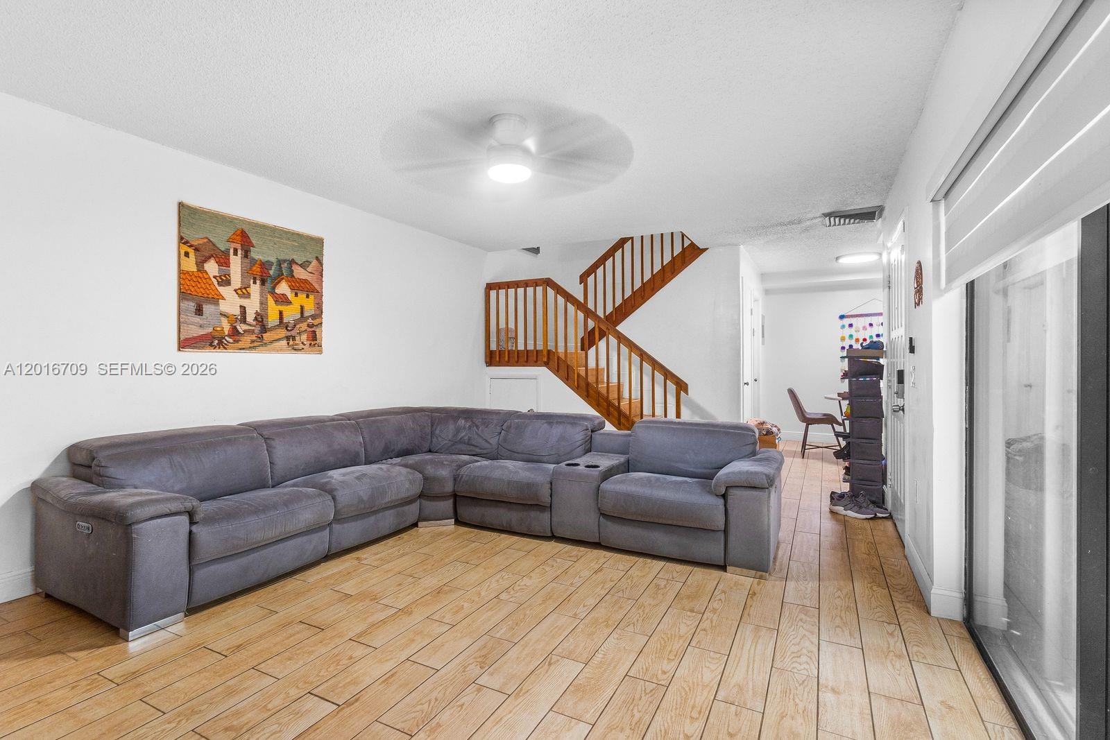 A living room features a large gray sectional sofa, wood-look tile flooring, and a staircase — 9126 SW 20th Pl # C, Davie FL 33324, DAVIE, FL
