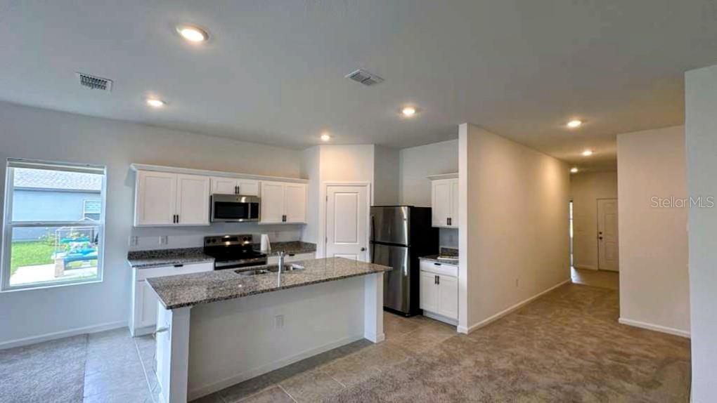 A kitchen with white cabinets, granite countertops, and stainless steel appliances opens to a carpeted area — 2449 GREY HAWK DR, KISSIMMEE, FL