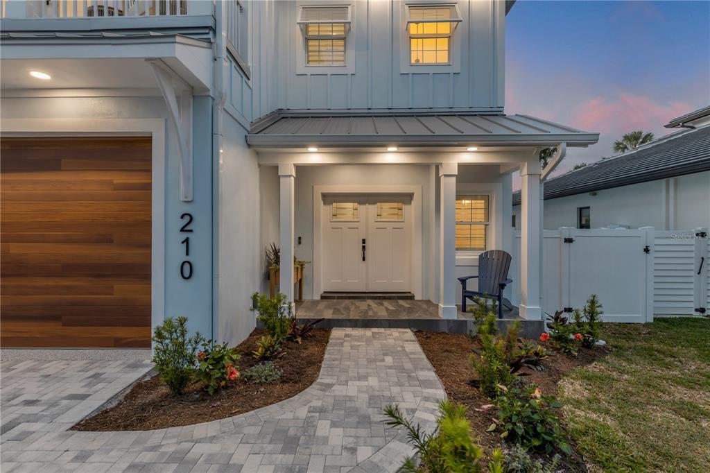 A paved walkway leads to the front entrance of a two-story house with white siding — 210 DUE EAST STREET, NEW SMYRNA BEACH, FL