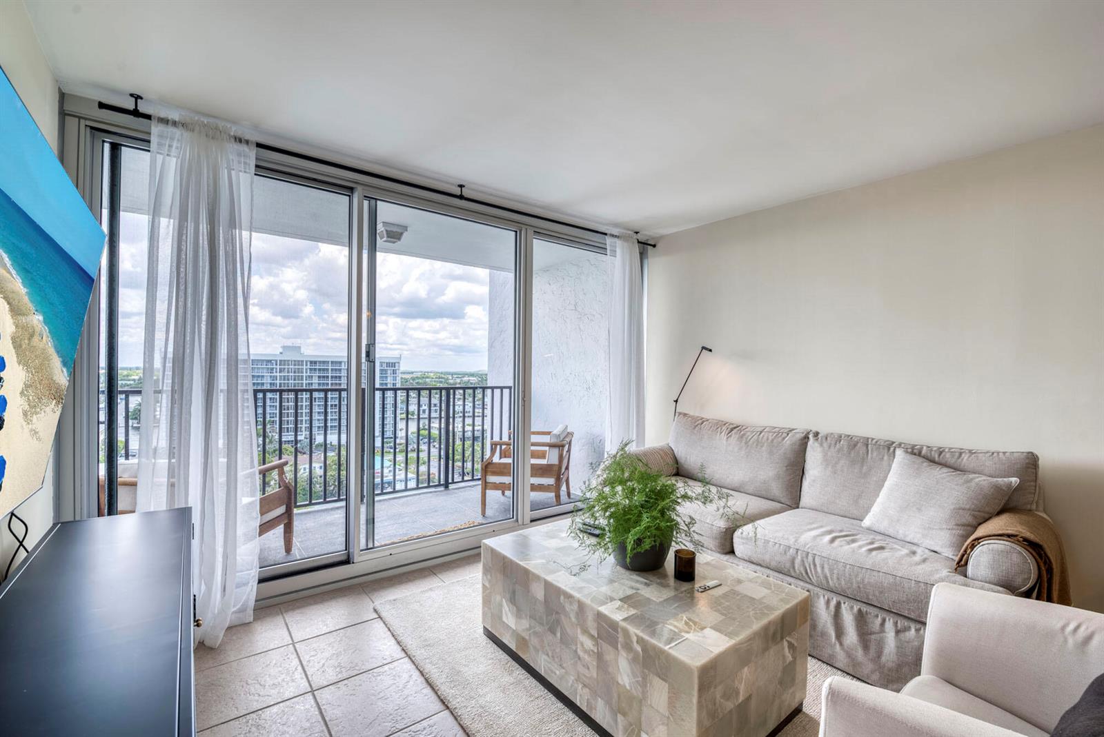 A living room features a beige sofa, stone coffee table, and sliding doors to a balcony — 525 N Ocean Boulevard # 1215, Pompano Beach FL 33062, POMPANO BEACH, FL