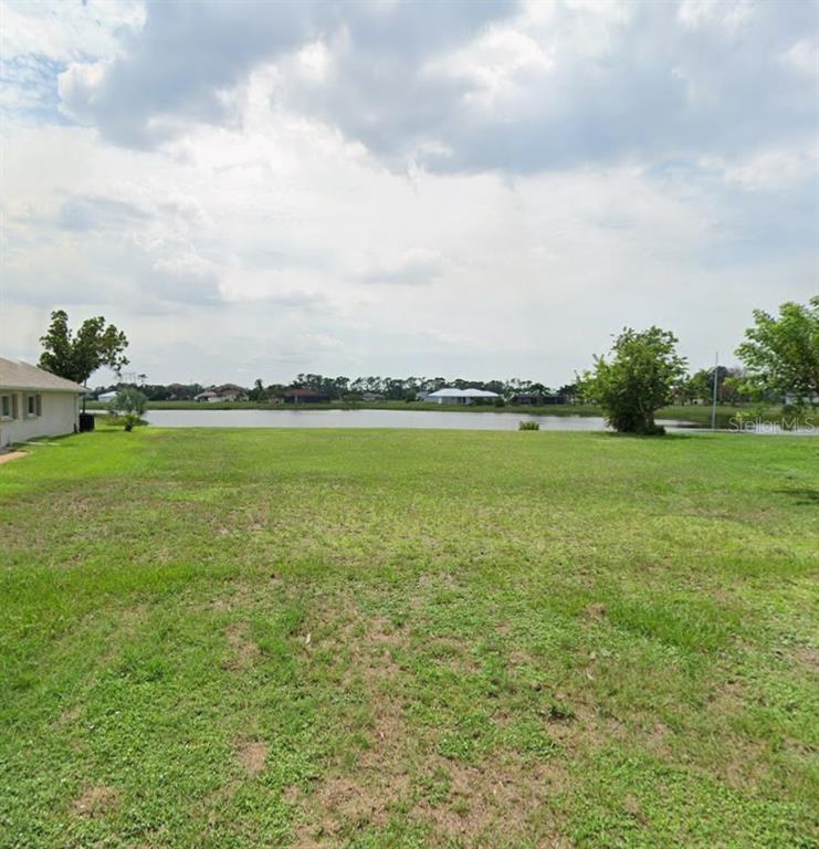 A grassy vacant lot overlooks a lake with houses in the distance — 17369 OPHIR LANE, PUNTA GORDA, FL