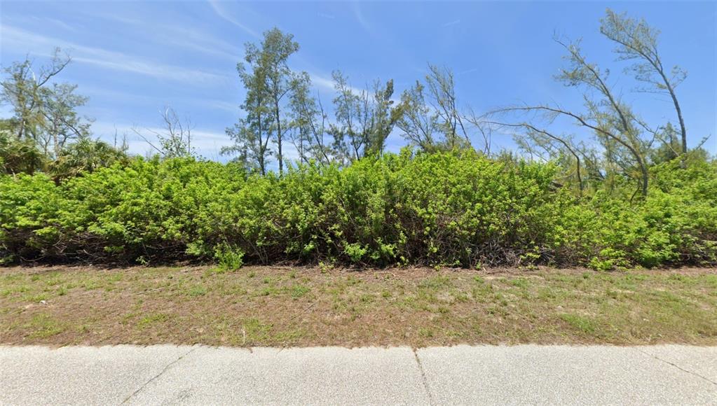 A vacant lot features a grassy foreground, dense green shrubs, and tall trees under blue sky — 10543 MANGROVE CIRCLE, PORT CHARLOTTE, FL